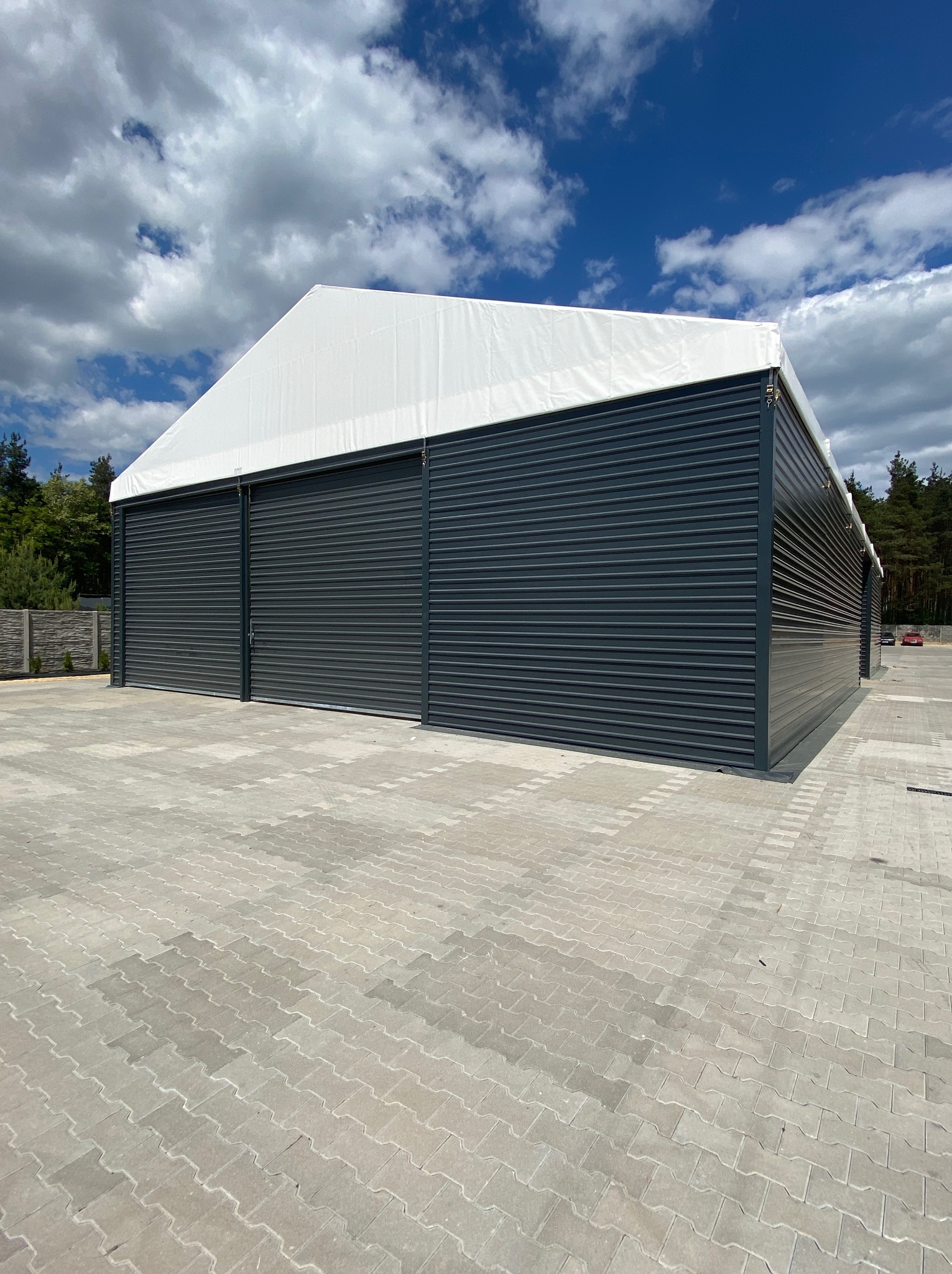 Gotowa hala magazynowa z rolowanymi drzwiami w Inowłodzu, z białą plandeką na dachu, na tle błękitnego nieba z chmurami.