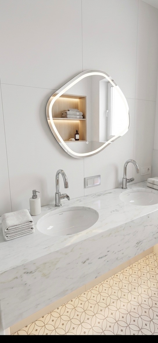 Nowoczesna łazienka z marmurowym blatem, dwoma umywalkami i podświetlanym lustrem o nieregularnym kształcie. W tle wnęka z półkami i ręcznikami.