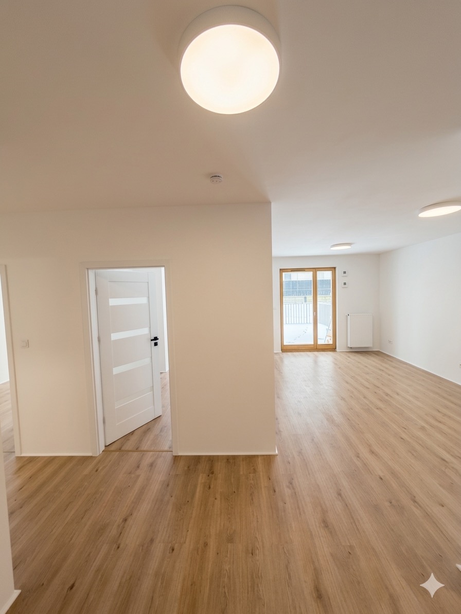Jasne, przestronne wnętrze po remoncie: drewnopodobne panele, białe ściany, drzwi z przeszkleniami i nowoczesne oświetlenie sufitowe. Widok na balkon.