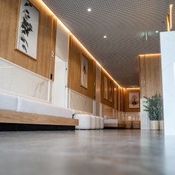 DentistiQ - Nowoczesna poczekalnia z drewnianymi panelami, marmurowymi akcentami, minimalistycznymi sofami i abstrakcyjnymi obrazami na ścianach, widziana z niskiej perspektywy.