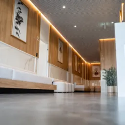 Nowoczesna poczekalnia z drewnianymi panelami, marmurowymi akcentami, minimalistycznymi sofami i abstrakcyjnymi obrazami na ścianach, widziana z niskiej perspektywy.