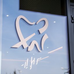 DentistiQ - Stylizowane logo zęba na szklanej fasadzie budynku z ciemną stolarką okienną i odblaskami neonów.