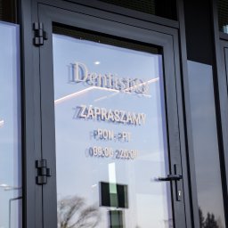 DentistiQ - Wejście do kliniki dentystycznej 'DentistiQ' z godzinami otwarcia wyklejonymi na szklanych drzwiach, widoczne metalowe zawiasy i klamka.