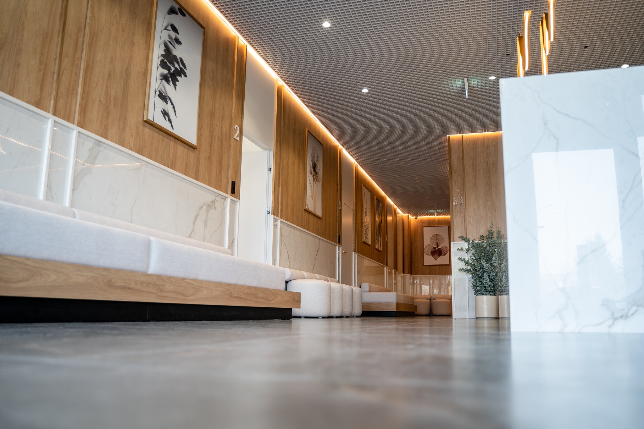 Nowoczesna poczekalnia z drewnianymi panelami, marmurowymi akcentami, minimalistycznymi sofami i abstrakcyjnymi obrazami na ścianach, widziana z niskiej perspektywy.