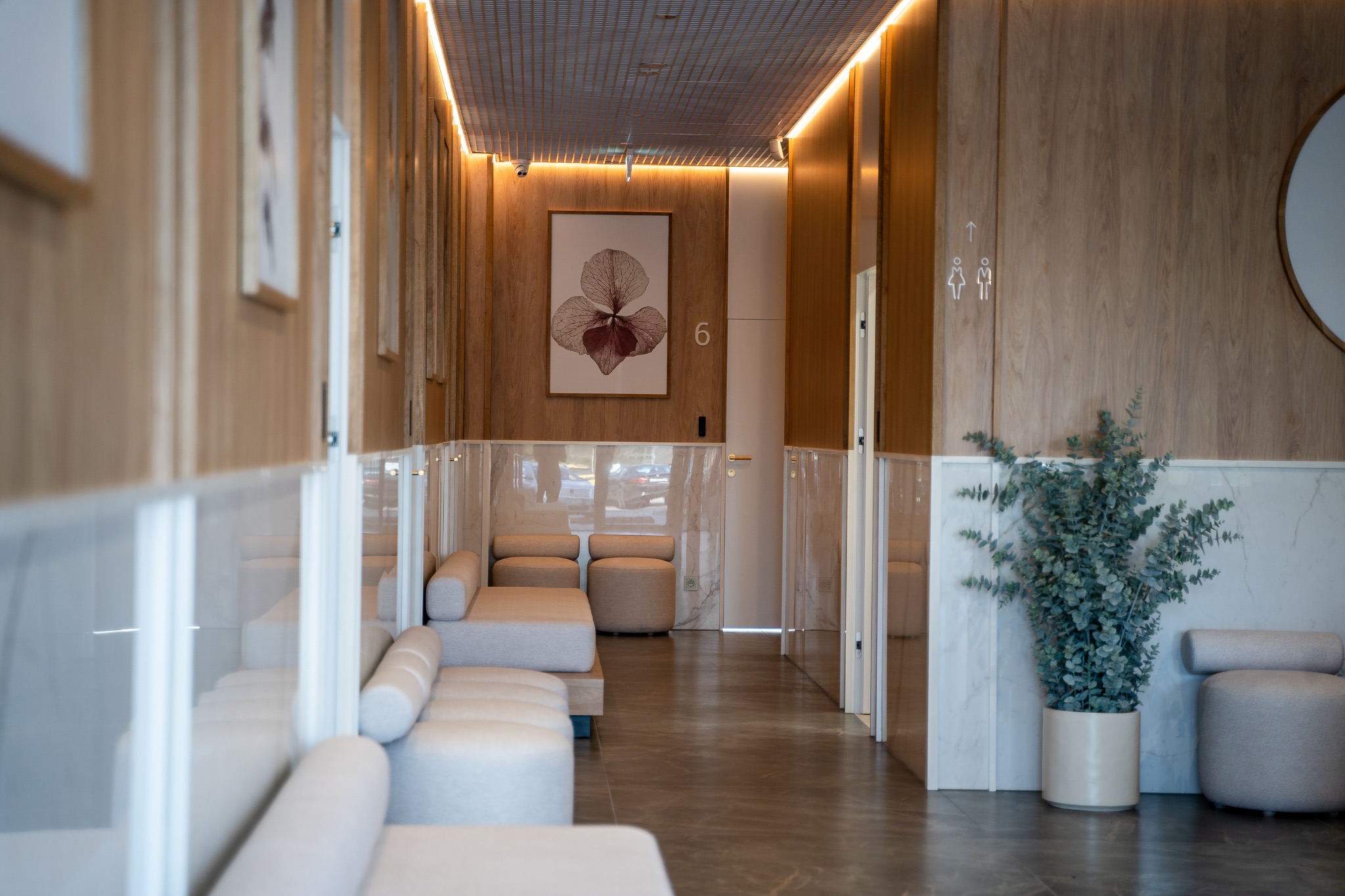 Wnętrze poczekalni w jasnej kolorystyce z drewnianymi panelami, obrazem orchidei na ścianie, rośliną w donicy i minimalistycznymi meblami.