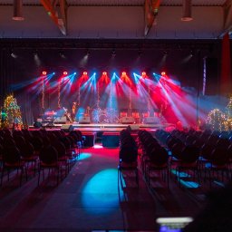 Wave Beats Karol Nadolski - Scena przygotowana do występu z instrumentami, perkusją, rzędami krzeseł dla publiczności i dekoracjami świątecznymi, oświetlona czerwonymi i niebieskimi reflektorami.