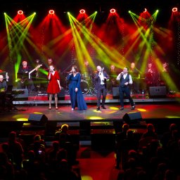 Wave Beats Karol Nadolski - Zespół muzyczny na scenie oświetlonej czerwonymi i zielonymi reflektorami, widownia w tle.