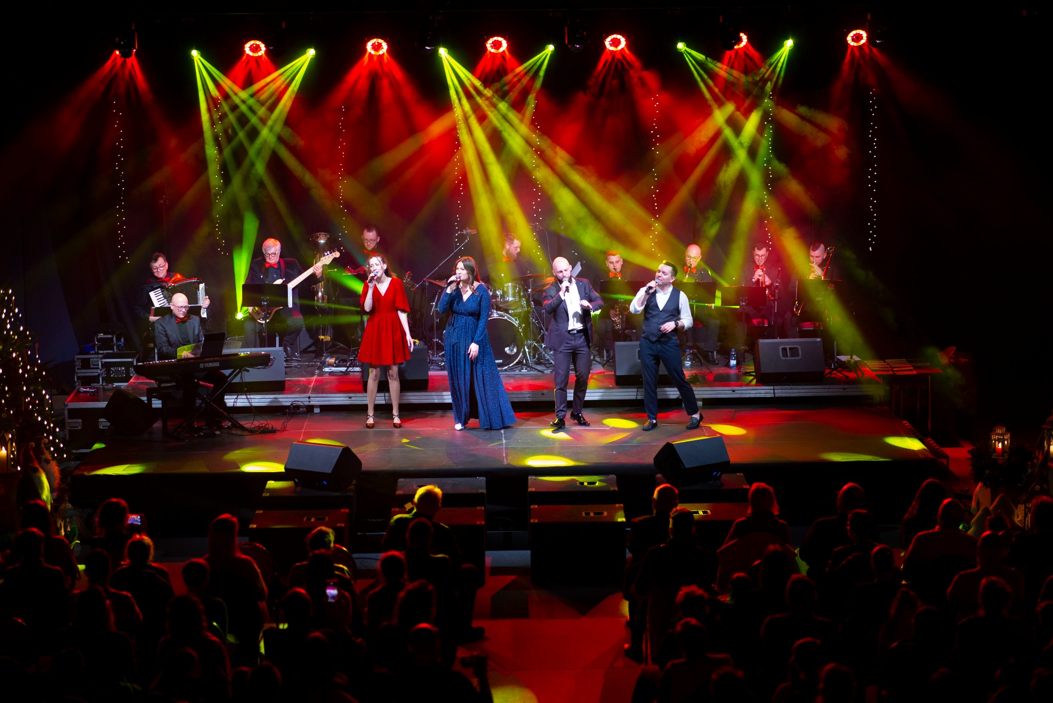 Zespół muzyczny na scenie oświetlonej czerwonymi i zielonymi reflektorami, widownia w tle.