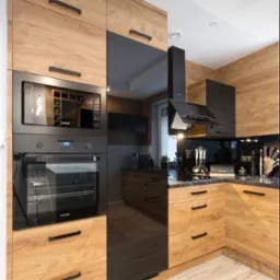 Nowoczesna kuchnia z drewnianymi frontami szafek i czarnymi, błyszczącymi elementami, zabudowany piekarnik i mikrofalówka marki Samsung, czarny okap i blat z ciemnego kamienia.