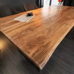 Stół z blatem z litego drewna o nieregularnym kształcie krawędzi, stylizowany na rustykalny, ustawiony w jadalni w Cerkwicy. Na blacie filiżanka kawy i gazeta.