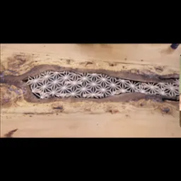 Drewniany blat stołu z żywicą epoksydową wypełnioną ażurowym wzorem geometrycznym, widoczne słoje drewna i naturalne pęknięcia.