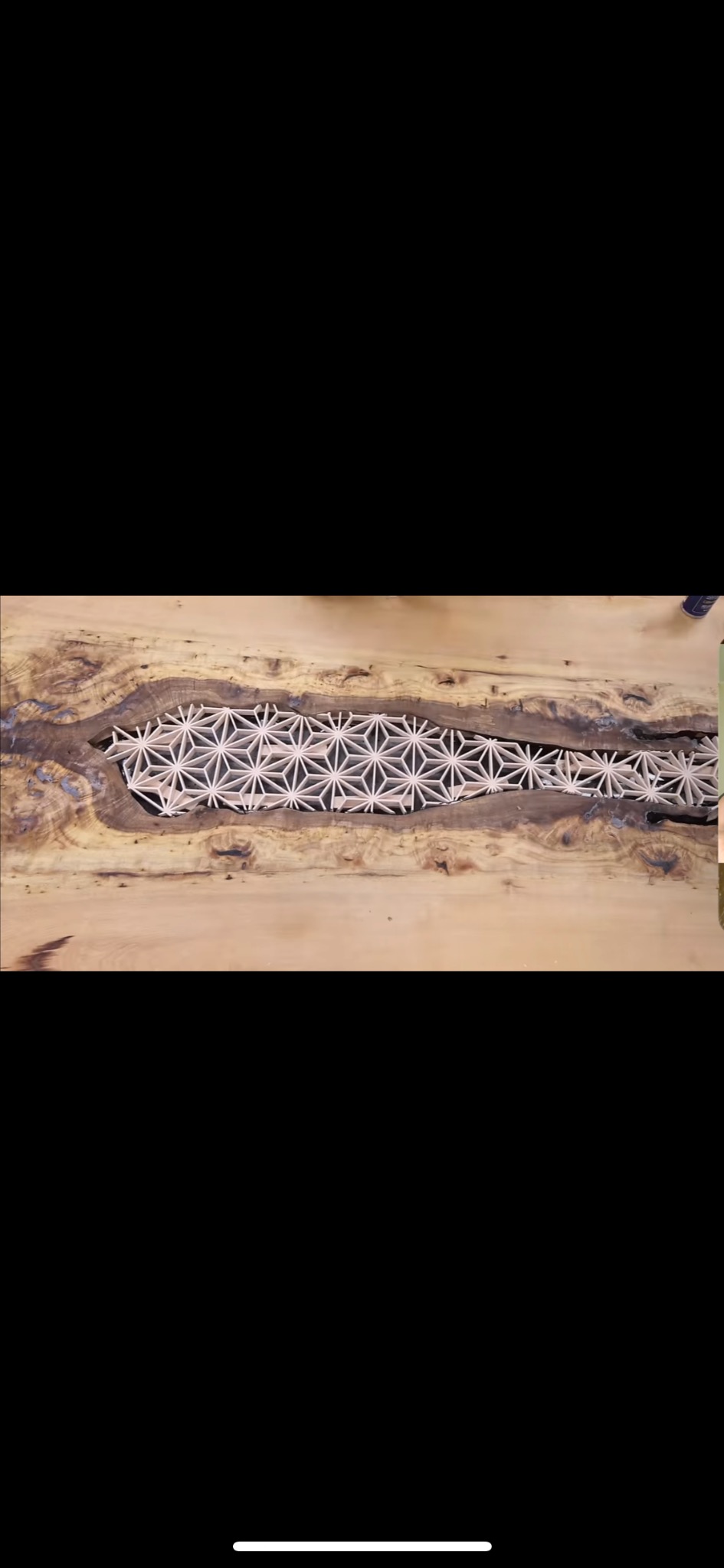 Drewniany blat stołu z żywicą epoksydową wypełnioną ażurowym wzorem geometrycznym, widoczne słoje drewna i naturalne pęknięcia.