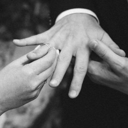 Andrii Kotelnikov - Czarno-białe zbliżenie dłoni zakładającej obrączkę na palec mężczyzny w garniturze.