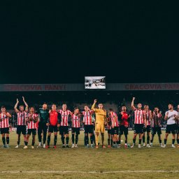 Andrii Kotelnikov - Drużyna piłkarska Cracovii świętuje zwycięstwo na stadionie, oświetlonym jupiterami, z widocznym telebimem nad trybunami.