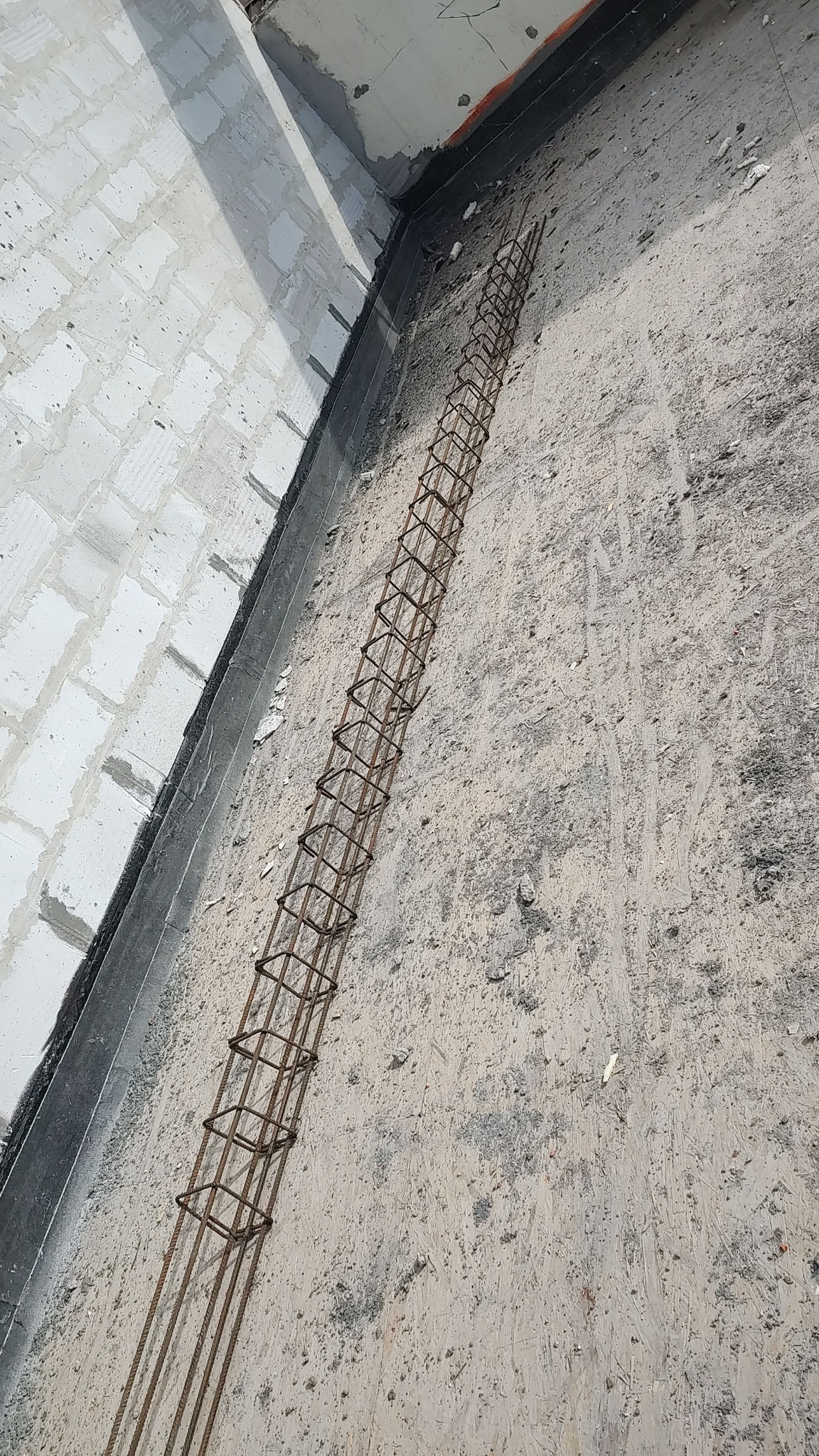 Zbrojenie w koszulce z prętów stalowych ułożone w rogu pomieszczenia na szalunku z płyty OSB, przygotowane do zalania betonem.