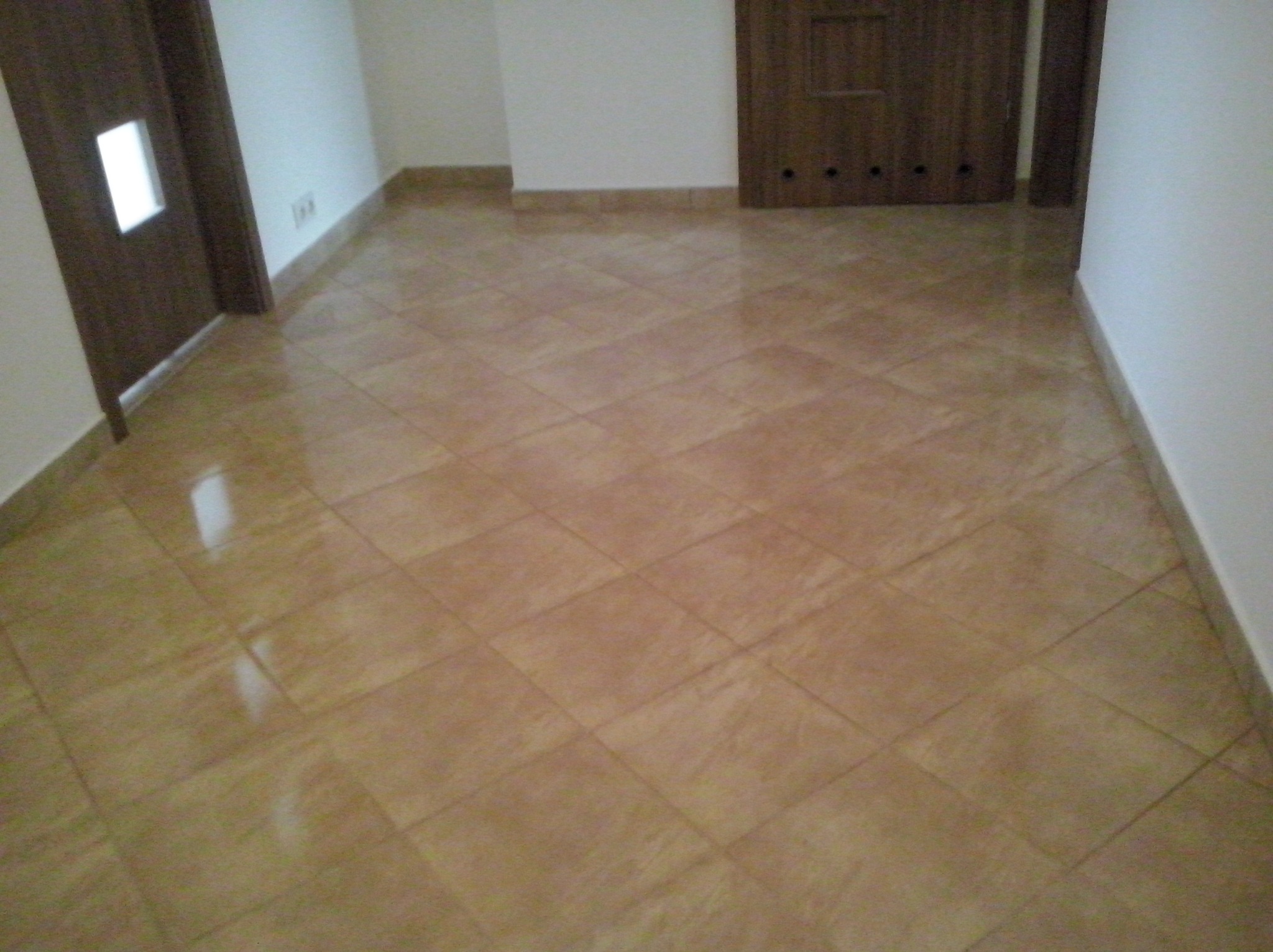 Ułożona pod kątem brązowa podłoga z płytek ceramicznych w jasnym pomieszczeniu, widoczne fragmenty drzwi i ściany.