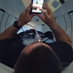 Osoba w komorze hiperbarycznej, z maską tlenową na twarzy, przegląda smartfon z otwartą aplikacją.