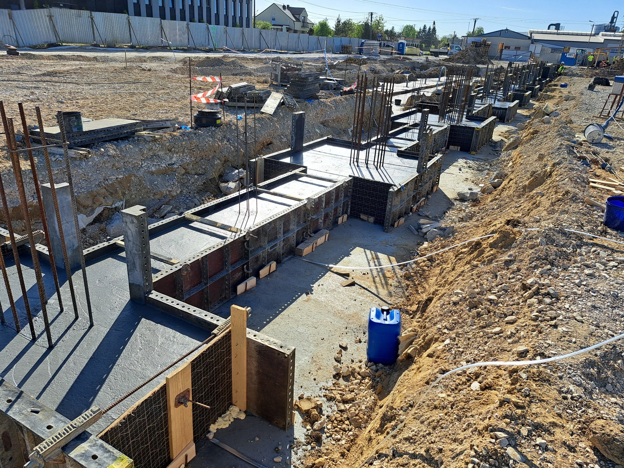 Wykop pod fundamenty zalany świeżym betonem, z widocznymi szalunkami i wystającymi prętami zbrojeniowymi, niebieski kanister w wykopie.