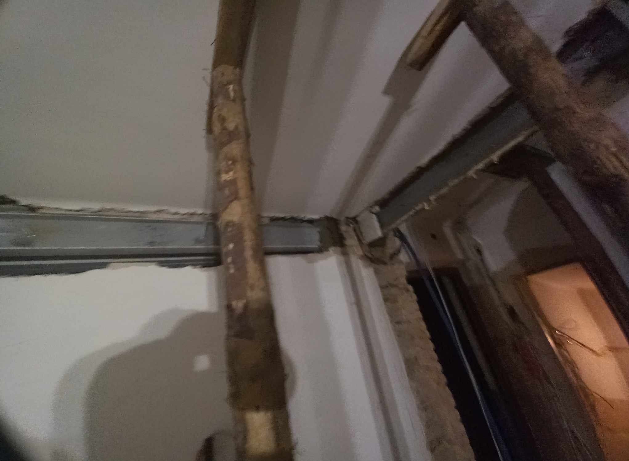 Wnętrze w trakcie prac rozbiórkowych, widoczne drewniane stemple podtrzymujące strop i odsłonięta stalowa belka nad otworem drzwiowym.