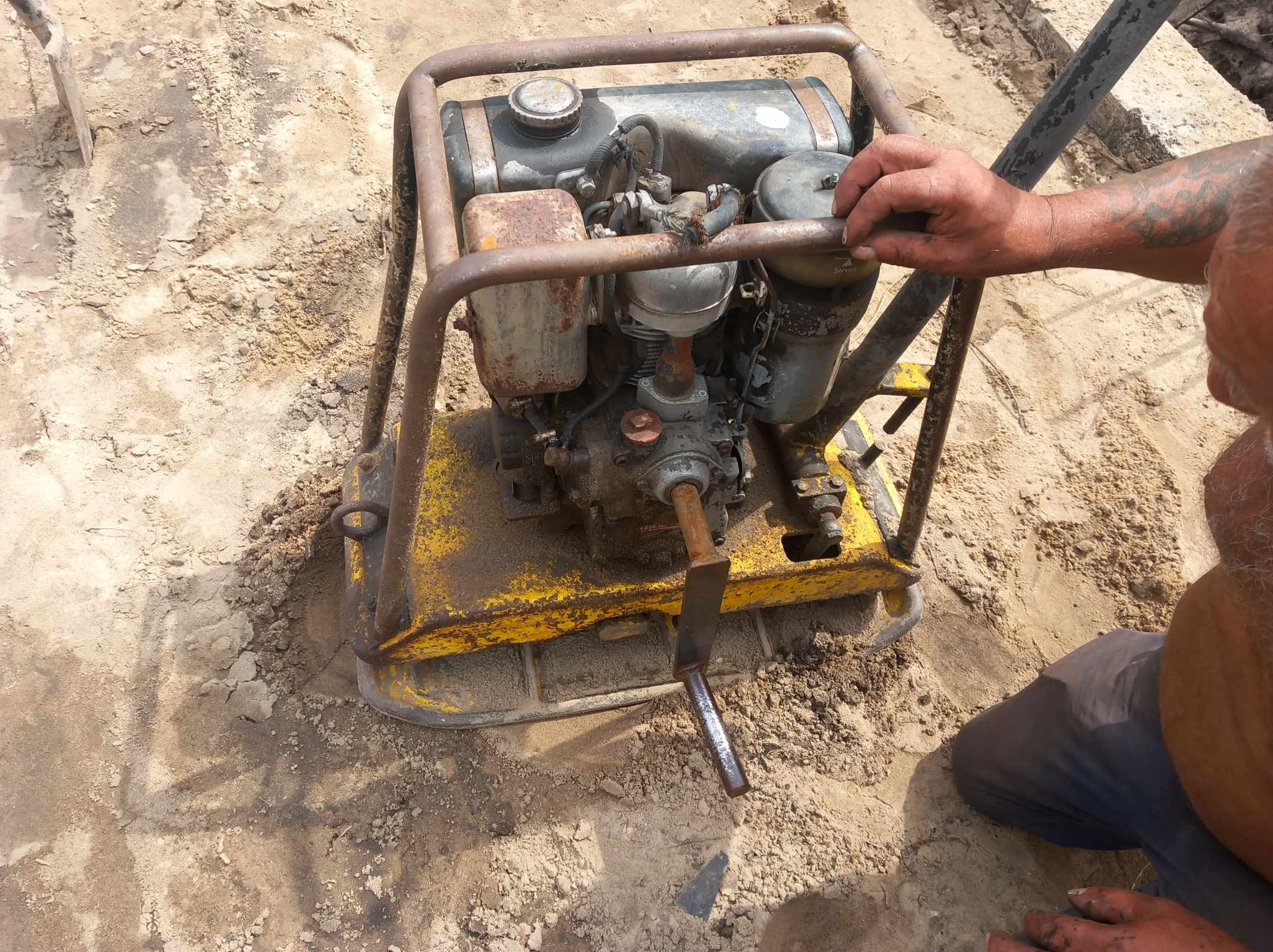 Operator obsługuje starą, żółtą zagęszczarkę gruntu podczas prac przygotowawczych pod fundamenty.