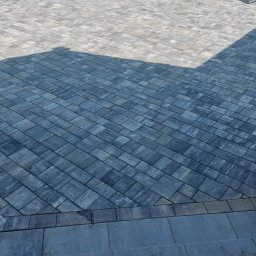 Pmbud - Ułożona kostka brukowa w szarych odcieniach, ułożona pod kątem, widoczne schody z kostki, w tle trawnik, drzewa i ogrodzenie.