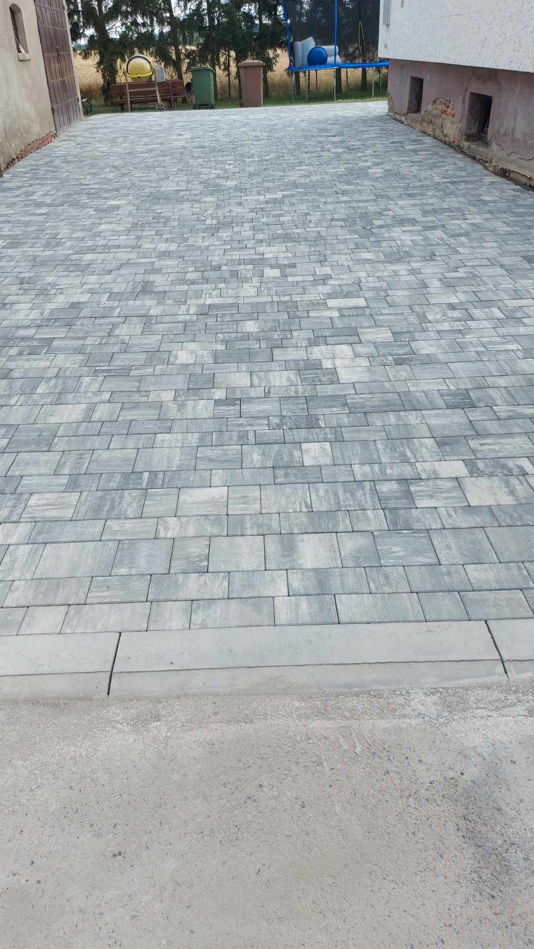 Ułożona szara kostka brukowa na podjeździe, widok z góry, obrzeża z szarego betonu.