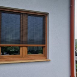 WOJCIECH FĄFARA BRAMSTEEL - Okno z drewnianą ramą i plisowaną roletą wewnętrzną, widok z zewnątrz na tle jasnej elewacji budynku i zaparkowanego samochodu z reklamą firmy.