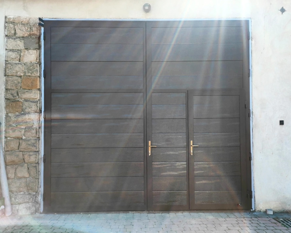Zewnętrzna brama z poziomymi panelami w kolorze ciemnego grafitu, z małym wejściem po prawej stronie, zamontowana między murem z kamienia a otynkowaną ścianą.