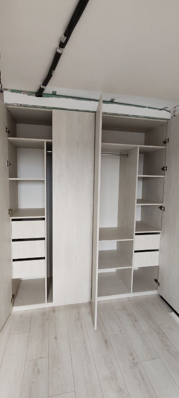 Wnętrze szafy wnękowej z jasnymi półkami i szufladami, widoczna instalacja elektryczna na suficie.