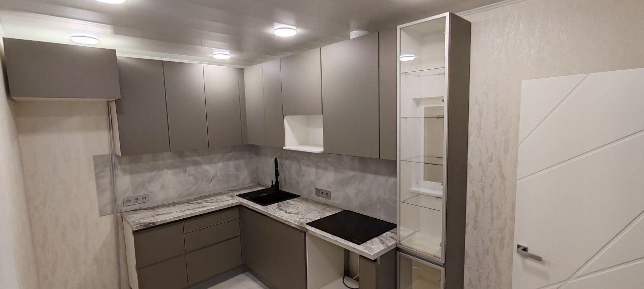 Nowoczesna kuchnia w odcieniach szarości z czarną armaturą, marmurowym blatem i przeszkloną witryną, widok na fragment białych drzwi z geometrycznym wzorem.