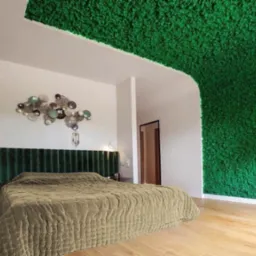 Sypialnia z łóżkiem z zielonym, mchem pokrytym fragmentem ściany i sufitu, oraz dekoracją ścienną w stylu boho.