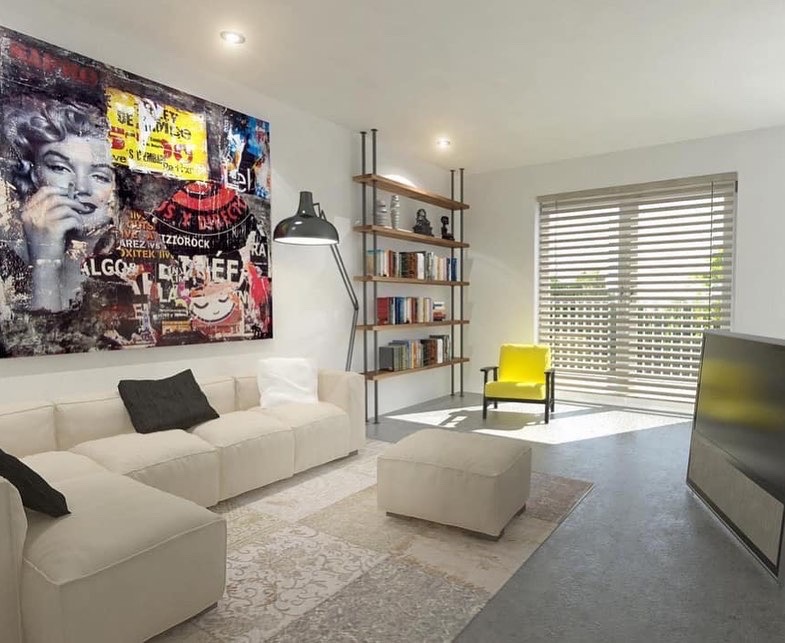 Jasny salon z narożną sofą, patchworkowym dywanem i dużą grafiką ścienną z wizerunkiem Marilyn Monroe, żółty fotel i regał na książki przy oknie z żaluzjami.