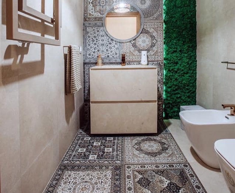 Nowoczesna łazienka z patchworkową podłogą, umywalką z szafką, okrągłym lustrem i zieloną ścianą z mchu.