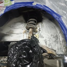 BREMS - Przygotowanie nadkola samochodu do zabezpieczenia antykorozyjnego, zakryte folią i taśmą, widoczny element zawieszenia.