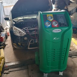 BREMS - Czarny samochód z otwartą maską na podnośniku warsztatowym, obok stoi zielone urządzenie do obsługi klimatyzacji samochodowej VIAKEN X540 z wyświetlaczem i manometrami.