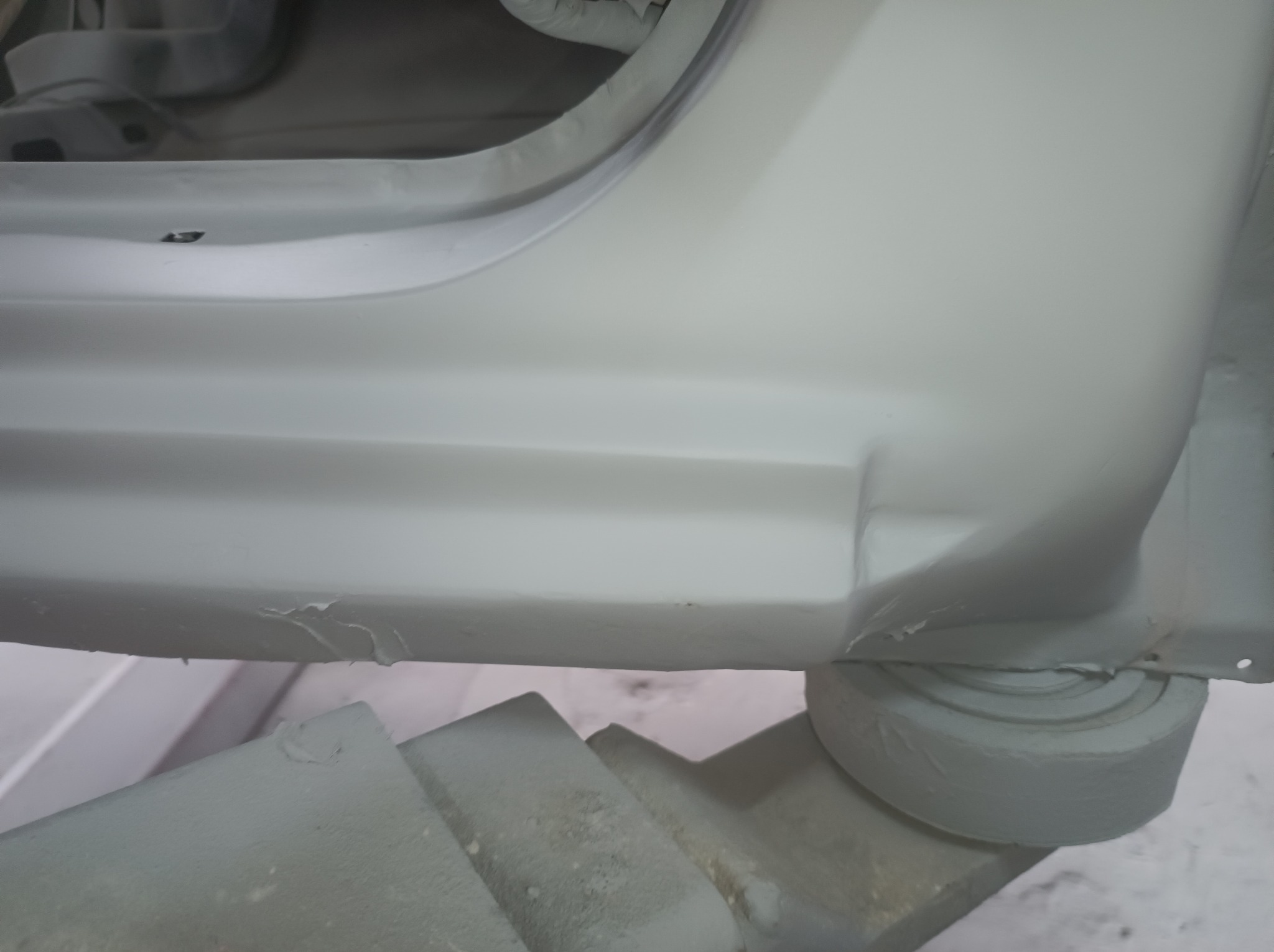 Fragment karoserii samochodu po naprawie blacharskiej, przygotowany do lakierowania, widoczne ślady szpachli i nierówności.