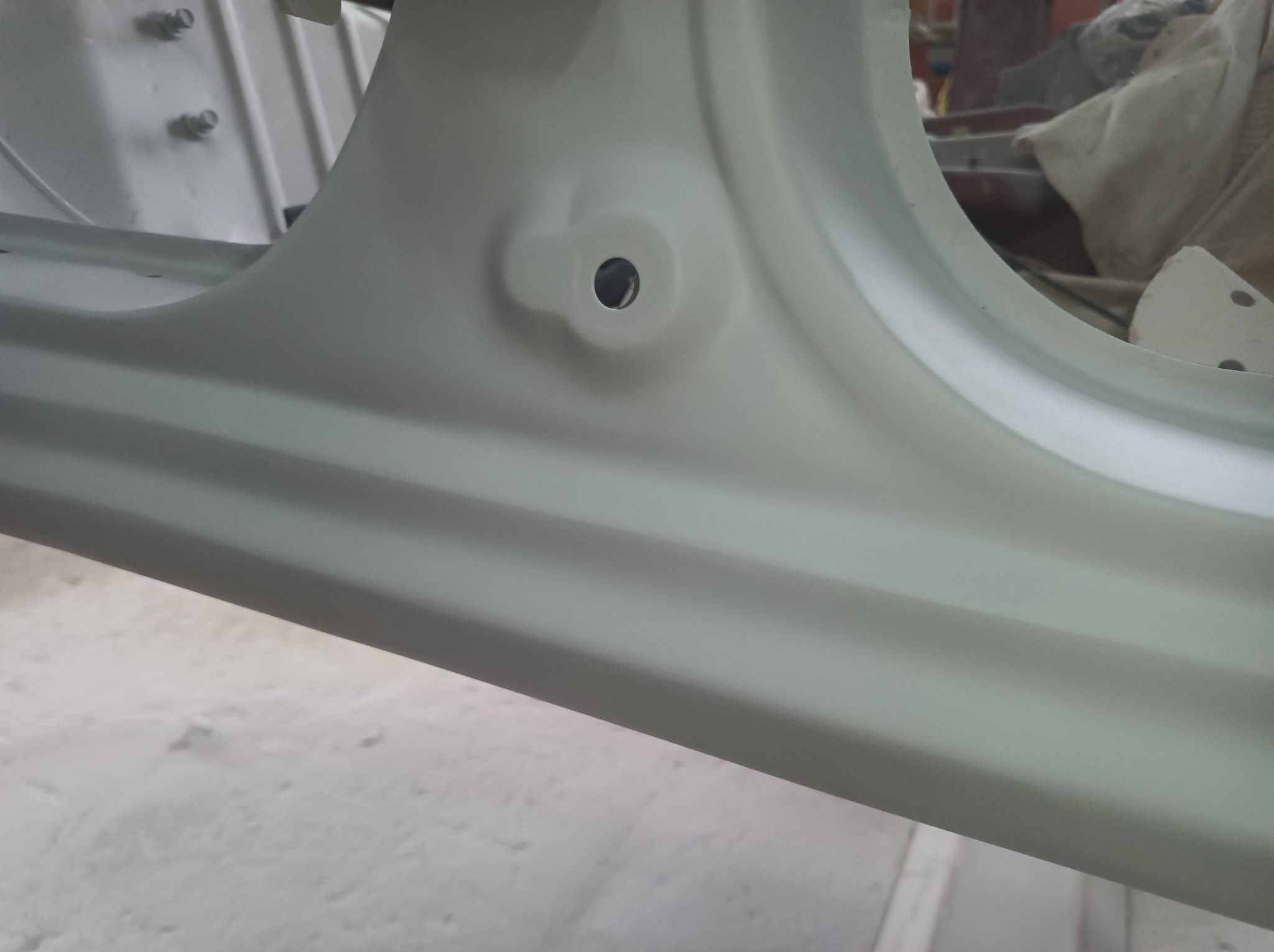 Fragment karoserii samochodu po piaskowaniu i nałożeniu podkładu, widoczny otwór montażowy i gładka powierzchnia przygotowana do dalszych prac lakierniczych.