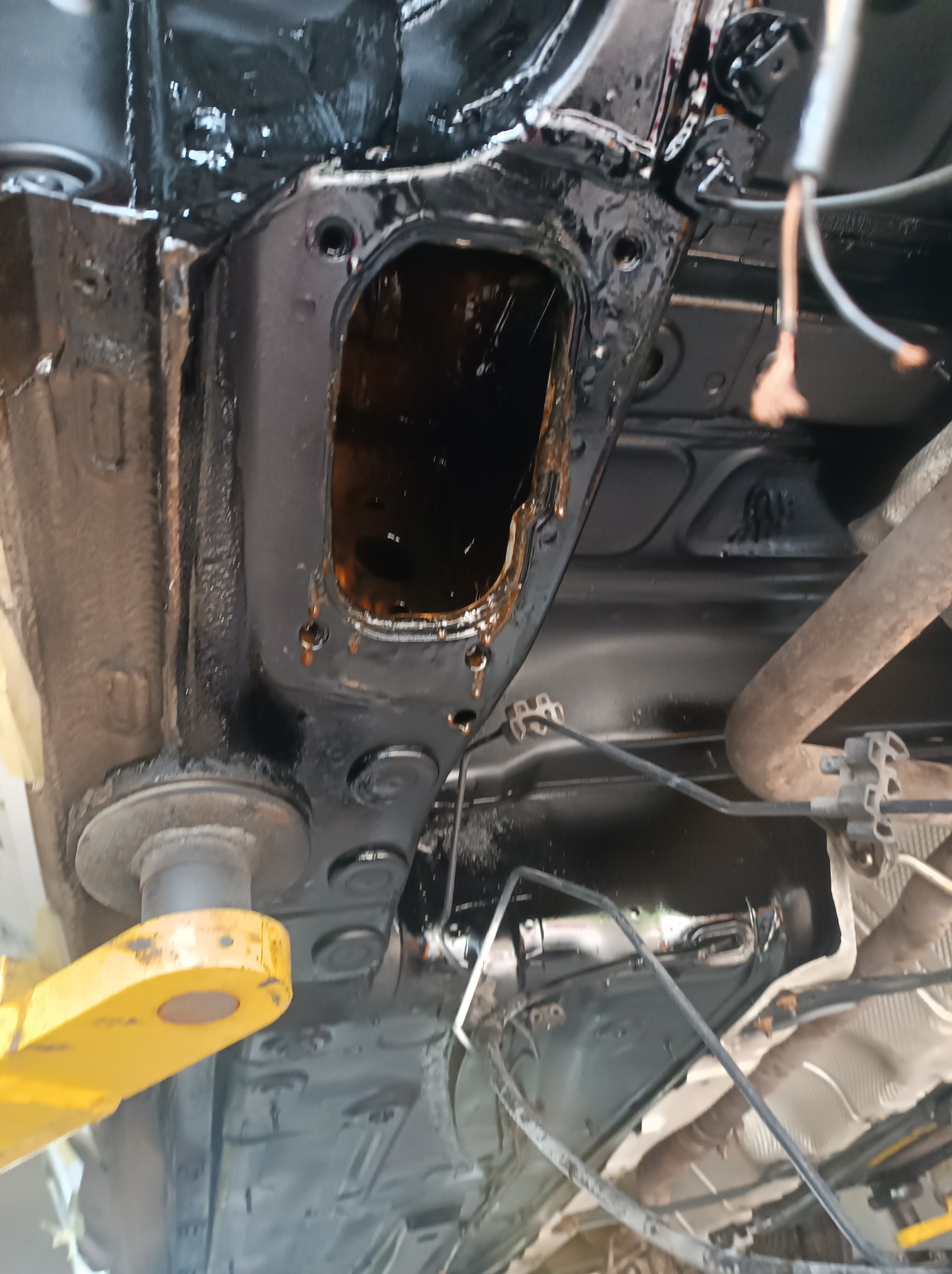 Podwozie samochodu na podnośniku, widoczne elementy po zabezpieczeniu antykorozyjnym, świecąca czarna powłoka i fragment układu wydechowego.