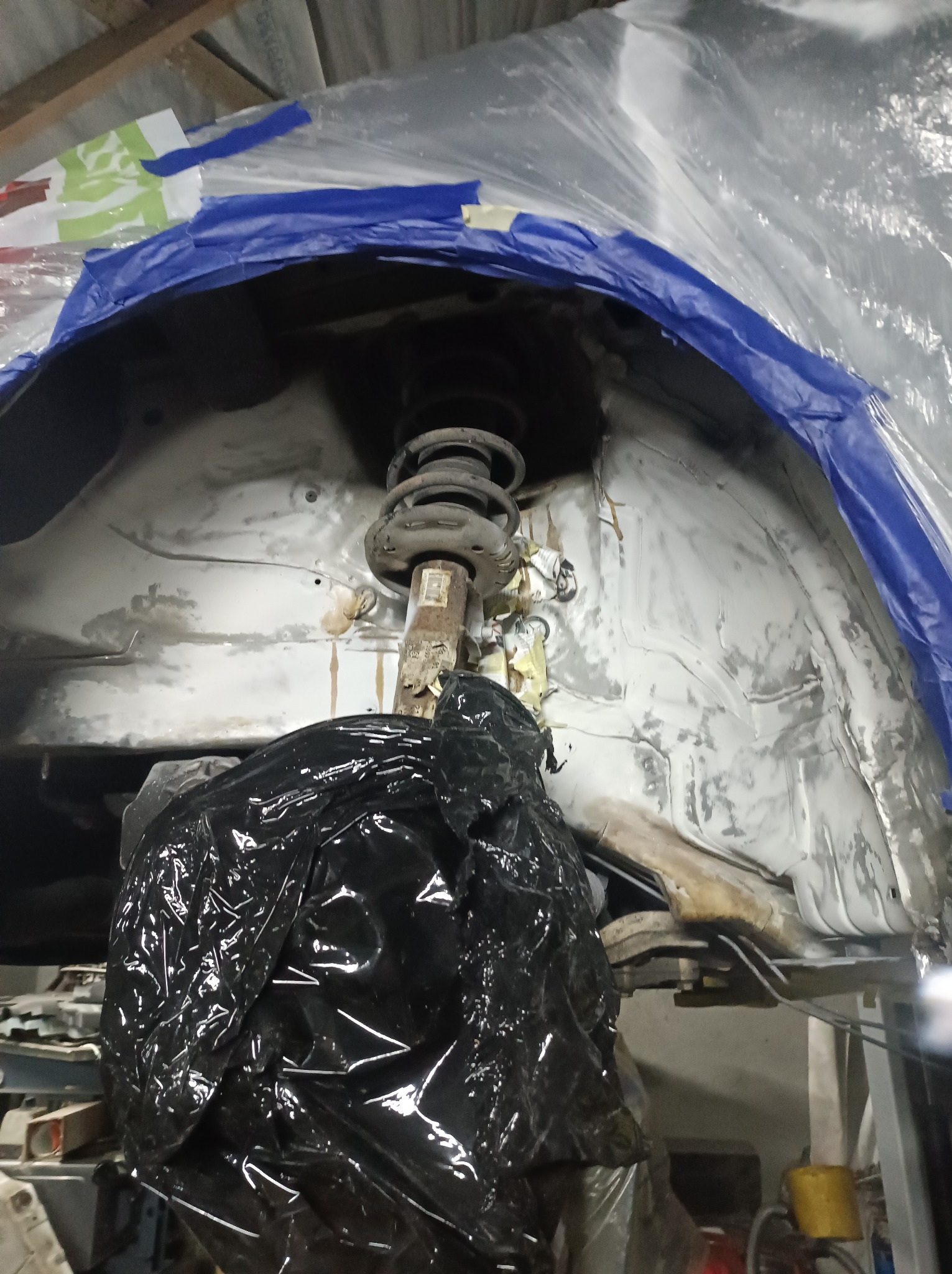 Przygotowanie nadkola samochodu do zabezpieczenia antykorozyjnego, zakryte folią i taśmą, widoczny element zawieszenia.