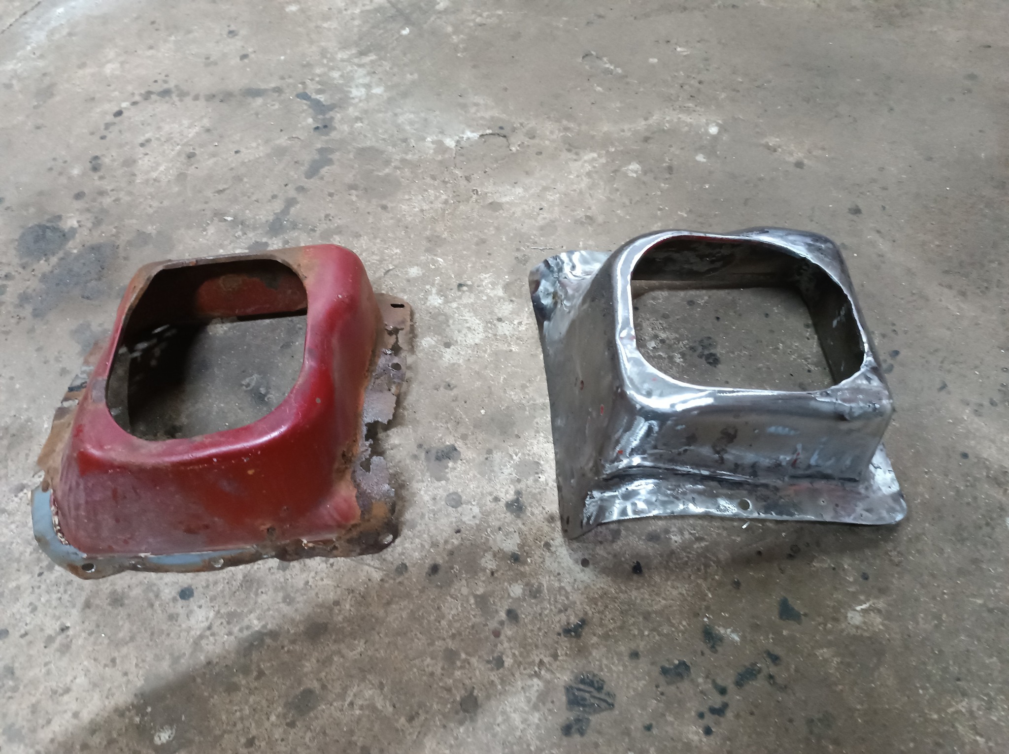 Dwa metalowe elementy samochodowe, jeden czerwony z widoczną korozją, drugi surowy metal po spawaniu, leżące na betonowej podłodze warsztatu.