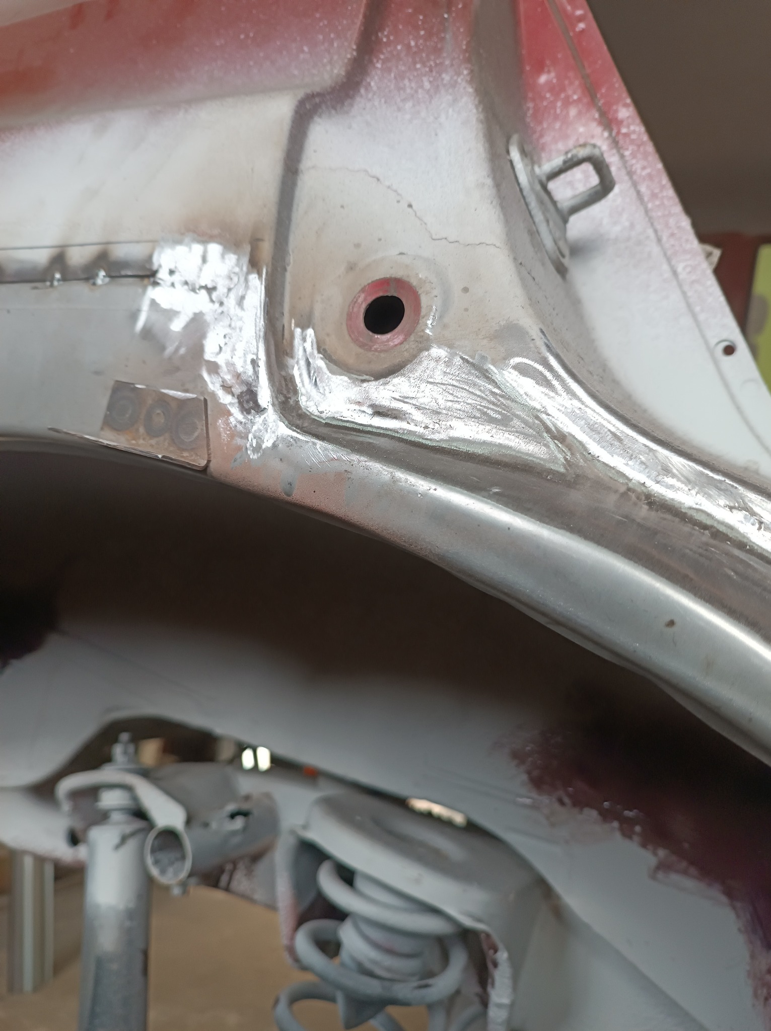 Fragment nadkola samochodu w trakcie naprawy blacharskiej, widoczne spawy punktowe i szlifowane powierzchnie przygotowane do lakierowania.