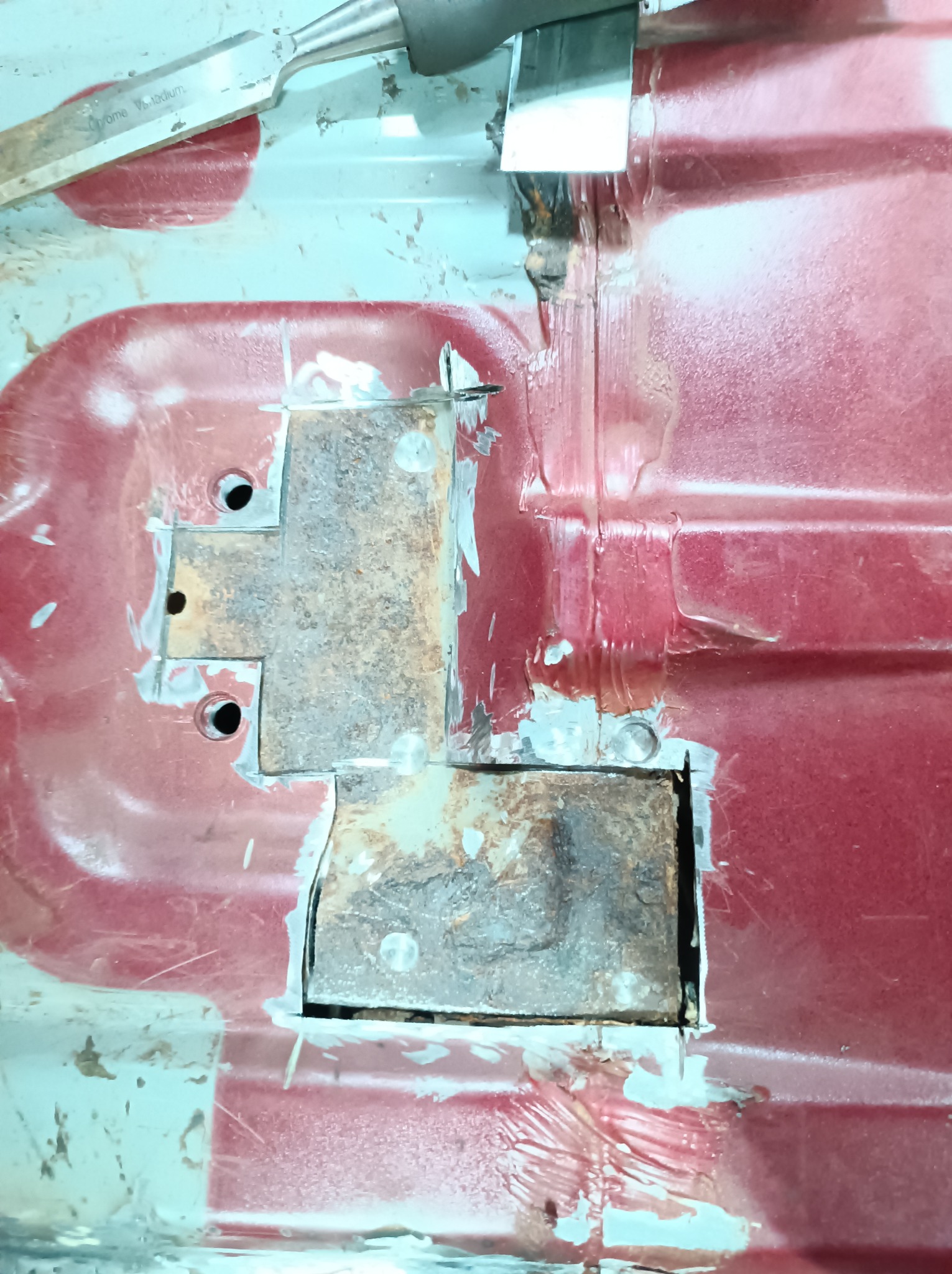 Fragment podwozia samochodu z wyciętymi skorodowanymi elementami i narzędziem w górnym rogu, przygotowywanymi do naprawy blacharskiej.