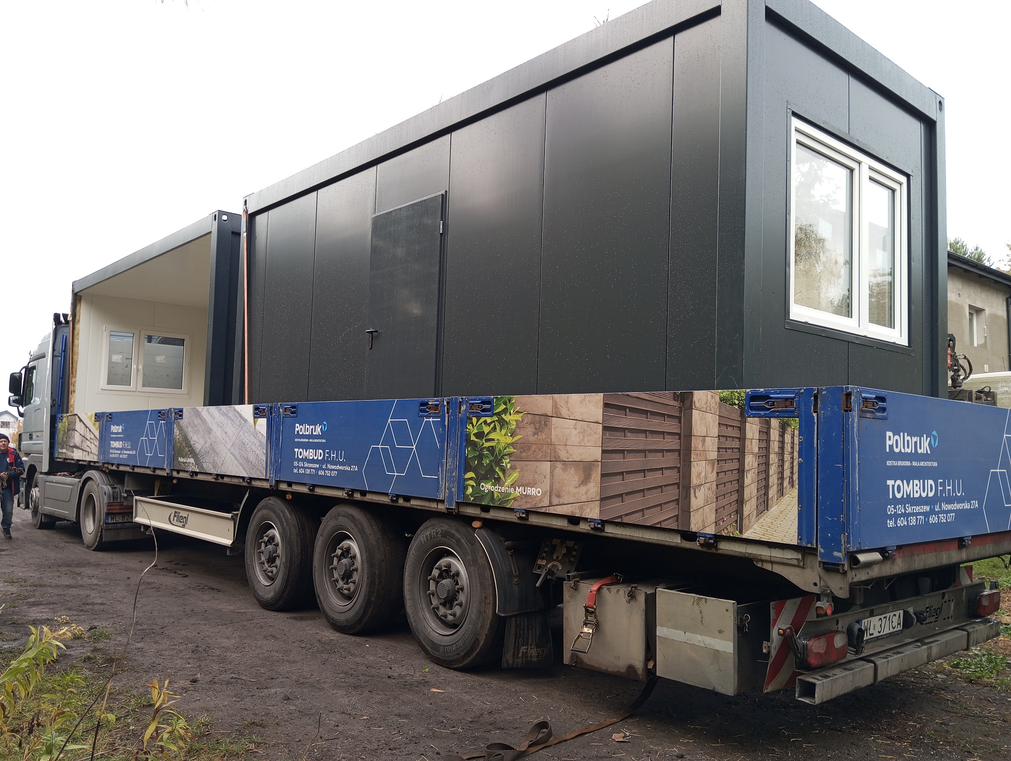 Transport dwóch modułowych segmentów na naczepie ciężarówki, widoczne okna i drzwi, reklama Polbruk na burtach naczepy.