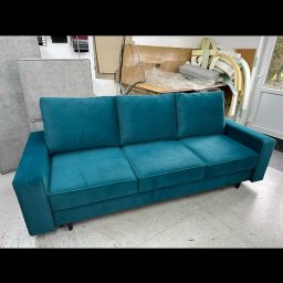 Leńmeble - Turkusowa sofa trzyosobowa z weluru w warsztacie tapicerskim, widoczne materiały i narzędzia w tle.