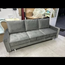 Leńmeble - Nowoczesna, szara sofa trzyosobowa z welurową tapicerką i minimalistycznymi nóżkami, sfotografowana w warsztacie tapicerskim z widocznymi materiałami i narzędziami w tle.