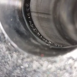 Wnętrze metalowej rury z widocznym spoiną po obwodzie, wykonaną metodą spawania, z efektem bokeh w tle.