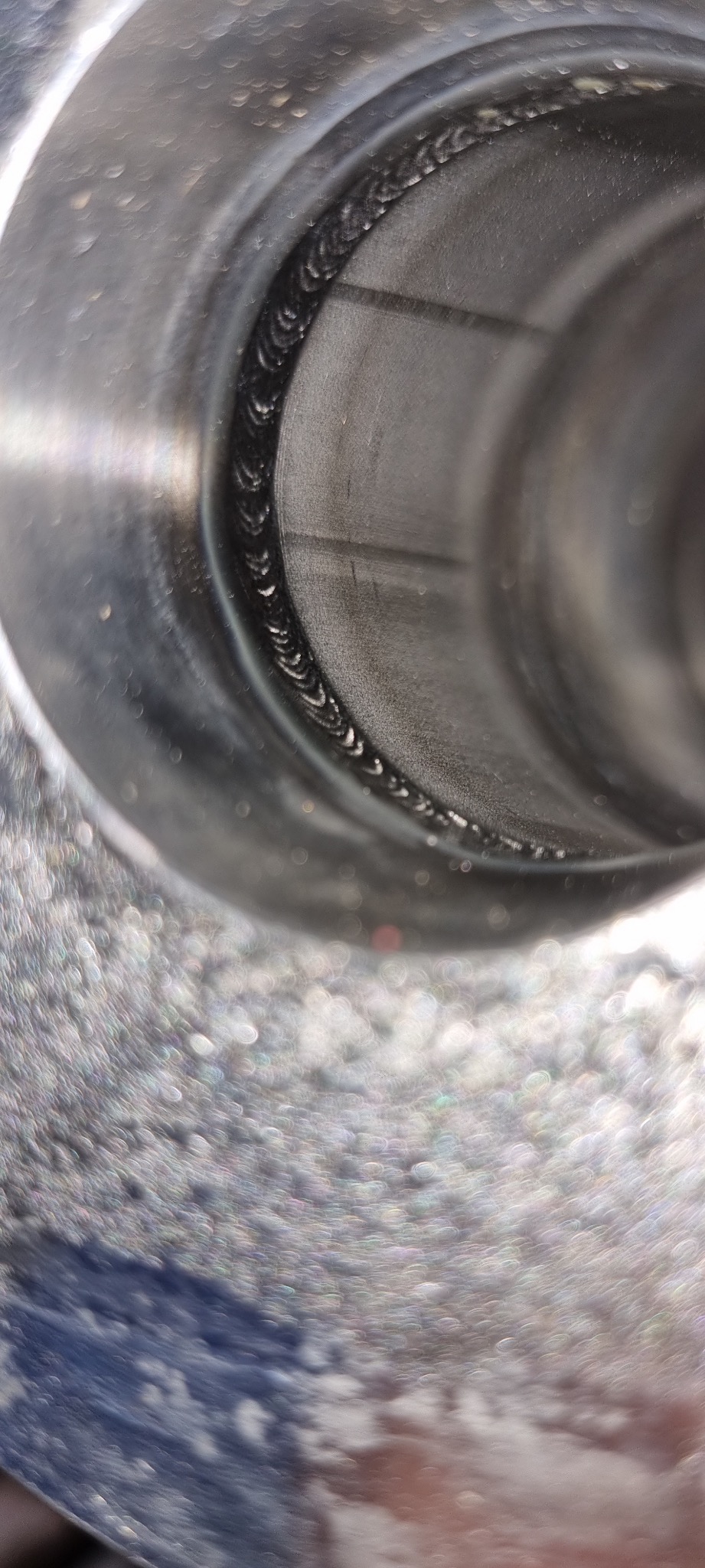 Wnętrze metalowej rury z widocznym spoiną po obwodzie, wykonaną metodą spawania, z efektem bokeh w tle.