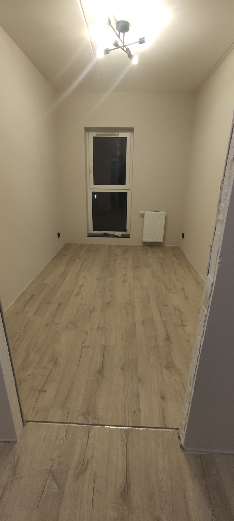 Jasne panele podłogowe w pustym pokoju z białymi ścianami i oknem, widok z progu drzwi.