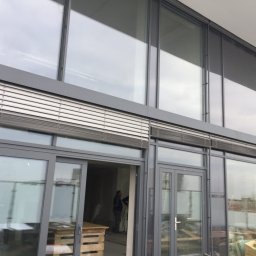 Perfect Windows Glazing Excellence - Duże aluminiowe okna fasadowe z żaluzjami zewnętrznymi, widoczne z zewnątrz budynku w trakcie prac wykończeniowych.
