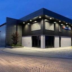 Perfect Windows Glazing Excellence - Nowoczesny budynek biurowy z aluminiową elewacją w odcieniach szarości, z oknami z żaluzjami i logo firmy na fasadzie, sfotografowany o zmierzchu.